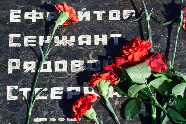Blumen am Denkmal für gefallene Soldaten, rote Nelken auf schwarzem Marmor, russischer Text über den militärischen Rang der Soldaten - Feldwebel, Major, Oberst, Oberstleutnant, Gefreiter, Unteroffizier - Foto, Bild