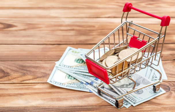 Shopping cart with coin and dollar bills on wooden table. - Photo, Image