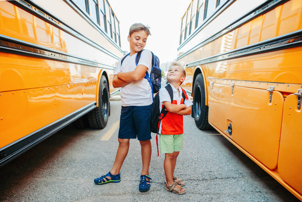 Szczęśliwi biali bracia studenci w pobliżu żółtego autobusu szkolnego. Uśmiechnięte dzieci wracające do szkoły we wrześniu. System edukacji i uczenia się. Wsparcie i przyjaźń.  - Zdjęcie, obraz