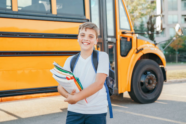 Happy Caucasian boy student with backpack and exrecise books near yellow bus on first September day. Education and back to school. Child kid ready to learn and study.  - Photo, Image