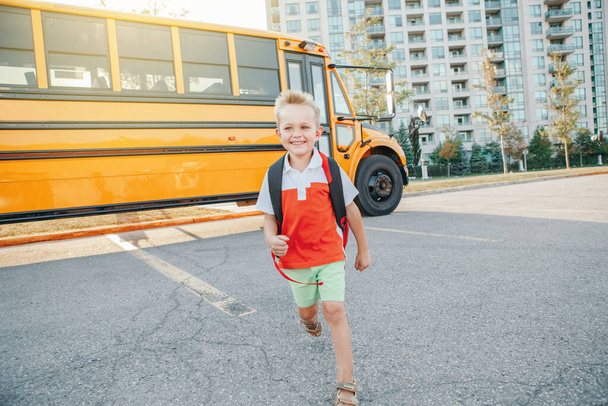 Šťastný usmívající se běloch, základní student běhající první zářijový den poblíž žlutého autobusu. Vzdělání a zpět do školy na podzim. Nadšený dítě na školním dvoře venku.  - Fotografie, Obrázek