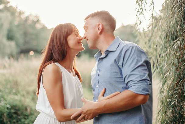 Beautiful smiling couple man woman in love. Boyfriend and girlfriend hugging in park on summer day at sunset. Togetherness and happiness. Authentic real people family outdoor.  - Photo, Image