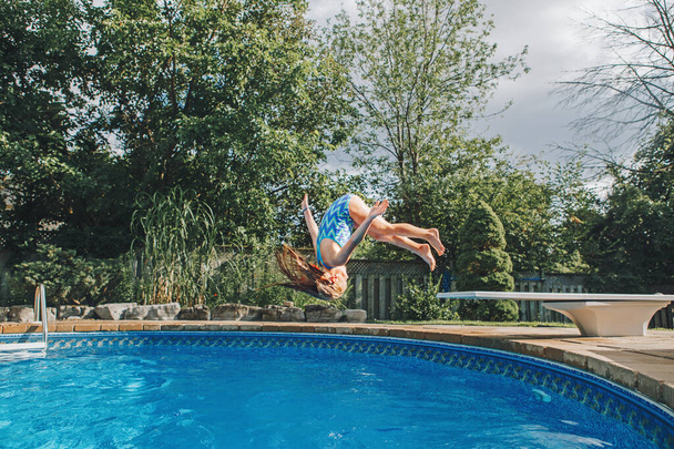 Menina de cabelos vermelhos bonito mergulho na piscina de trampolim. Criança gosta de se divertir na piscina no quintal de casa. Atividade de água ao ar livre de verão para crianças.  - Foto, Imagem