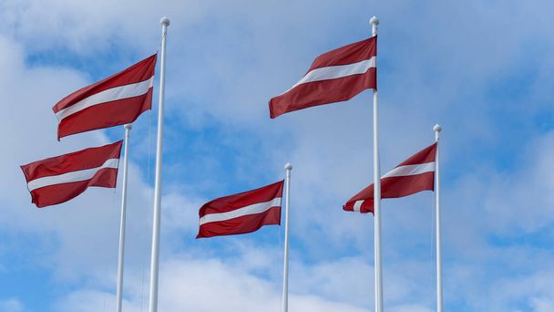 Letonya Bayrakları Mavi Gökyüzüne Karşı Rüzgarda Dalgalanıyor. Mavi ve Bulutlu Arkaplanda Letonya Bayrağı Güçlü Rüzgarda Dalgalanıyor. Letonya Ulusal Bayrağı. - Fotoğraf, Görsel