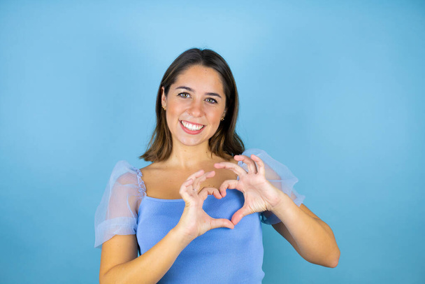 Mladá krásná žena přes izolované modré pozadí s úsměvem v lásce ukazující symbol srdce a tvar s rukama - Fotografie, Obrázek