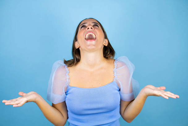Young beautiful woman over isolated blue background crazy and mad shouting and yelling with aggressive expression and arms raised - Foto, immagini