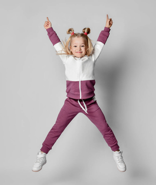 Cheerful baby girl in a stylish modern pink gray sports hoodie and pants jumps high. - Fotoğraf, Görsel