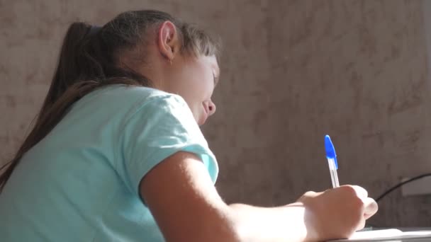 Het kind schrijft lessen. Tienerschoolmeisje maakt huiswerk door notities op te schrijven in een notitieboekje. Het concept afstandsonderwijs. Student, schoolmeisje meisje is bezig met zelfopvoeding zitten aan huis tafel. - Video