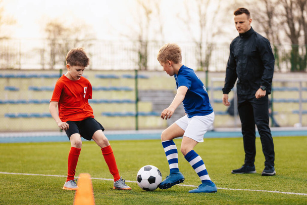 Νεαρά αγόρια στην προπόνηση ποδοσφαίρου με τον προπονητή. Οι μικροί ποδοσφαιριστές διαγωνίζονται στην εκπαιδευτική μονάδα. Νεαρός προπονητής προπονεί παιδιά αθλητικής σχολής. Στάδιο ποδοσφαίρου σχολείο σε θολή φόντο - Φωτογραφία, εικόνα