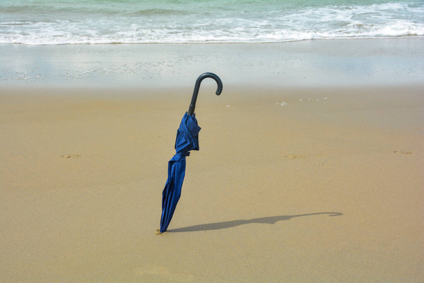 Un paraguas cerrado está atascado en la arena, en la playa a la luz del sol - Foto, Imagen