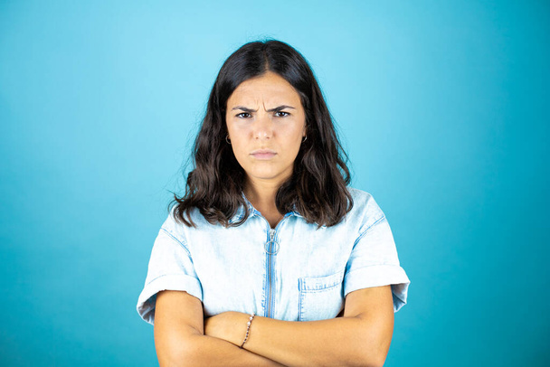 Young beautiful woman wearing a denim jumpsuit over isolated blue background looking tired and bored with crossed arms. - Photo, Image