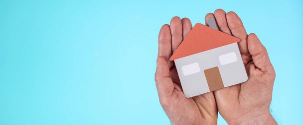 Έννοια της ασφάλισης στο σπίτι με χάρτινο σπίτι στα χέρια σε γαλάζιο φόντο - Φωτογραφία, εικόνα