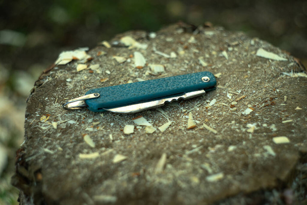 Bolsillo, cuchillo plegable de color azul se encuentra en una pieza de madera en las virutas - Foto, imagen