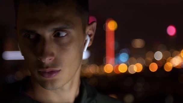 Young man in earphones looking around at night - Footage, Video