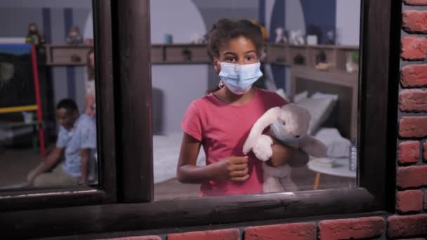 Dark-skinned schoolgirl in medical mask by window - Video