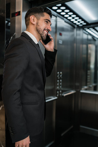 Portrait of young businessman talking on the phone at the hotel elevator. Business travel concept. - Valokuva, kuva