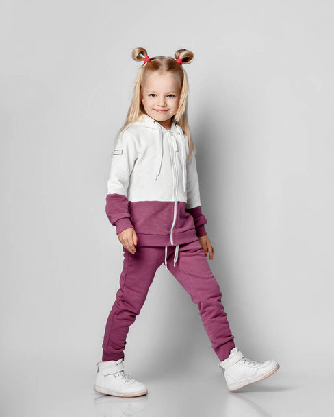 Little blonde girl in a sports suit posing on a gray background. - Foto, immagini