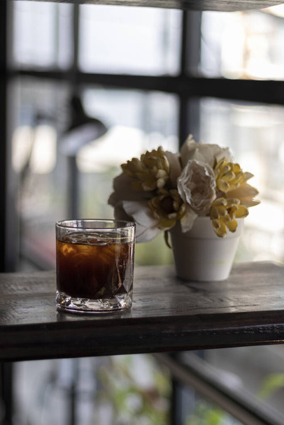 Een verticaal shot van ijskoffie en bloemen op een houten tafel - Foto, afbeelding