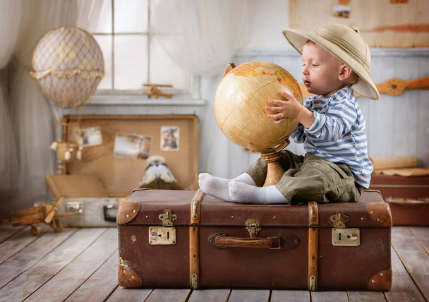 Little boy is like a traveler and plays with a globe sitting on a suitcase - 写真・画像