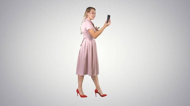Young woman in pink holding using smart phone recording video blog while walking on gradient background. - Foto, afbeelding