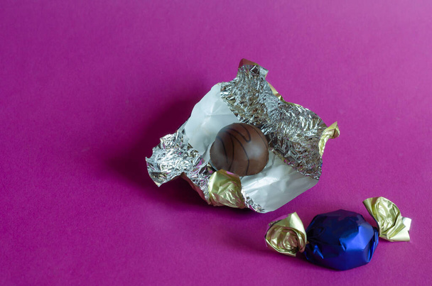 Két csokis cukorka rózsaszín háttérrel. Csomagolós és csomagolás nélküli édességek. Édes csemege. Másold a helyet. Szelektív fókusz. - Fotó, kép