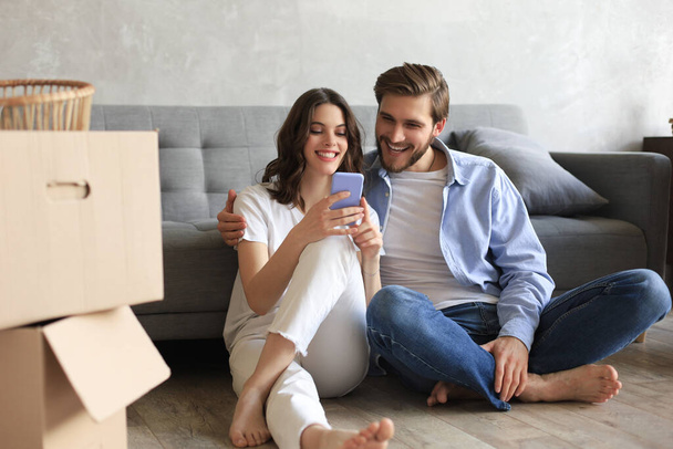 Happy couple sitting and planning new home decoration at home with a smartphone at moving day, renovation and interior design for new house. - Фото, зображення