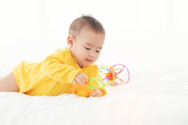 Cute noworodka tajskie zabawy w łóżku. Małe dziecko w pieluszce leżące na brzuchu na białym łóżku z zabawkami - Zdjęcie, obraz