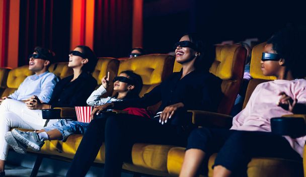Group of people watch movie with 3D glasses in cinema theater with interest looking at the screen, exciting and eating popcorn - Фото, изображение