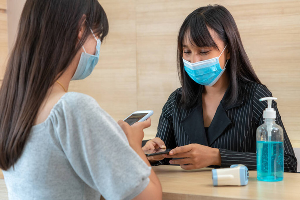 Receptionist and guest wearing face mask at front desk while having conversation in office or hospital . Covid 19 and coronavirus infection protection and protective policy concept . - Foto, Imagen