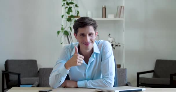 Cheerful smiling boss business man wears classic shirt, sits at table, shows two thumbs up, puts like, shows approval support, symbol of agreement, sign of positive verdict good decision, look camera - Video