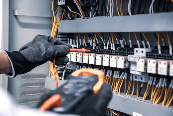 Digitális multi-métert használó villamosmérnök mérőberendezéssel ellenőrzi az áramerősséget az áramkör megszakítónál és a kábelvezetéket a fő áramelosztó táblán. - Fotó, kép