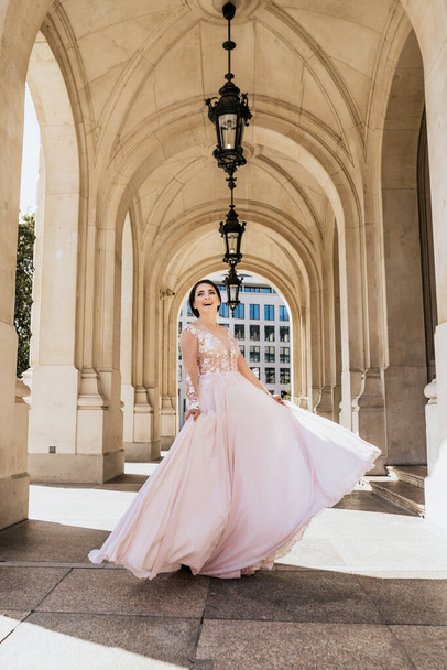 Krásná atraktivní žena v dlouhých růžových šatech. Mladá žena tanec s budovou pozadí - Fotografie, Obrázek