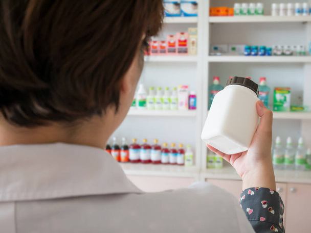 Female pharmacist hold medicine bottle on her hand in the pharmacy store - Фото, изображение