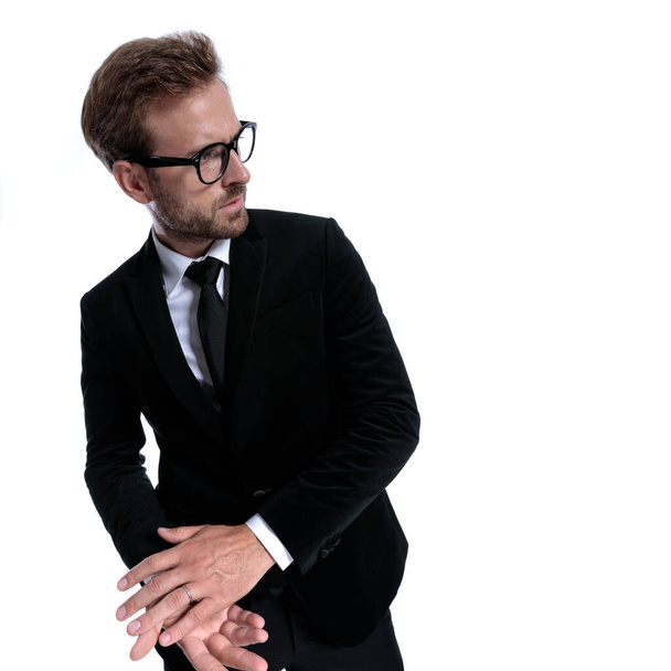 cool elegant businessman in black suit looking to side, anxiously rubbing palms, standing isolated on white background - Photo, Image