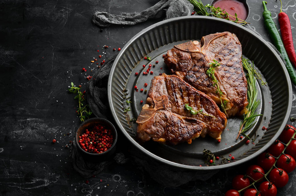 Grilled T-bone steak with spices in a metal baking dish on a black background. Top view. Rustic style. - Foto, Imagem