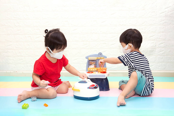 cute babies wearing protective mask sitting on the floor pretend play food toy.Children's kitchen game.  - Photo, Image