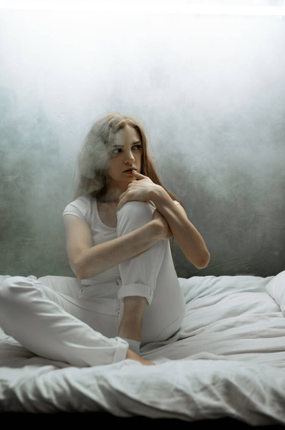 Τρελή γυναίκα με μαξιλάρι στο κρεβάτι, σκοτεινό δωμάτιο στο βάθος. Ψυχεδελικό άτομο με προβλήματα κάθε βράδυ, κατάθλιψη και άγχος, θλίψη, ψυχιατρικό νοσοκομείο - Φωτογραφία, εικόνα