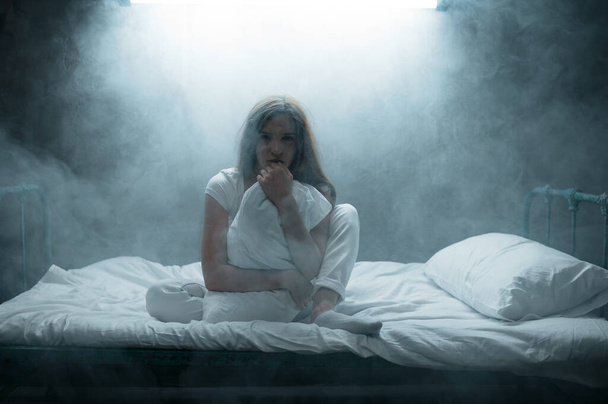 Szalona kobieta z poduszką siedząca w łóżku, ciemny pokój na tle. Psychodeliczna osoba mająca problemy każdej nocy, depresja i stres, smutek, szpital psychiatryczny - Zdjęcie, obraz