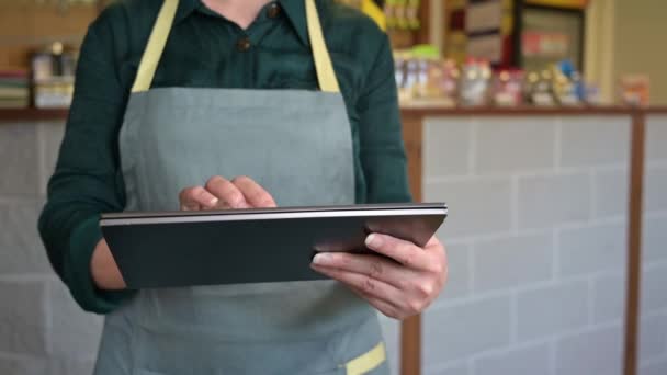 vrouwelijke ober neemt een bestelling van een klant met behulp van een tablet in een klein cafe. - Video