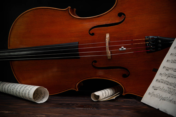 Cello leží na dřevěném povrchu s lukem a hudebním stojanem. Místo pro text - Fotografie, Obrázek