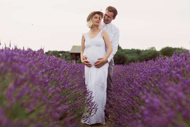 The pregnant wife with her happy husband is standing in a hug in the lavender field - Foto, Imagem