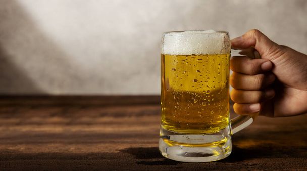 Masada bir bardak birayla el ele tutuşmak. Gün içinde evde ya da kafede bira içmek - Fotoğraf, Görsel