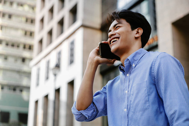 Sonriente joven asiático hombre de negocios utilizando el teléfono móvil en la ciudad - Foto, imagen