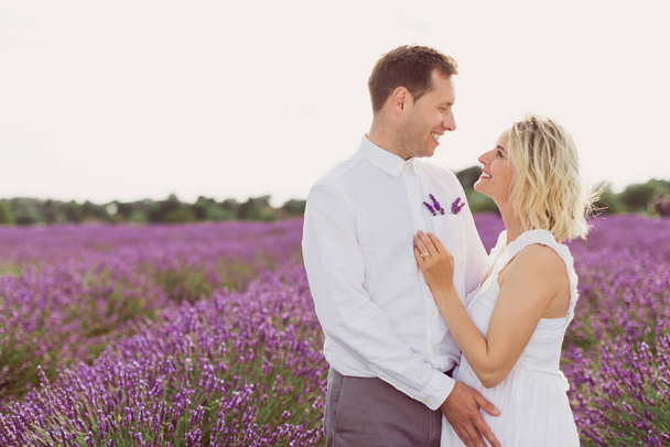 The happy young man hugging his attractive pregnant wife in the lavender field and looking at her - Fotó, kép
