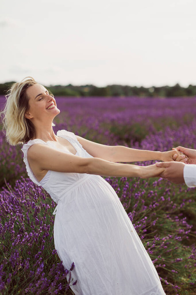 The happy pregnant woman standing in the lavender field and holding hands her husband - Foto, afbeelding