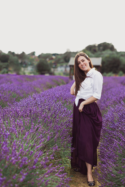 Beautiful young brunette is standing in a lavender field - Fotografie, Obrázek