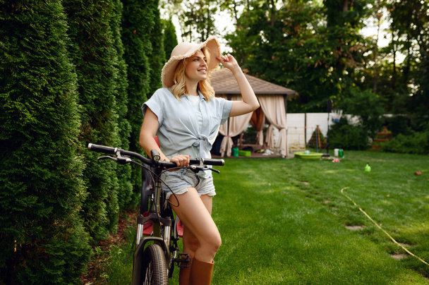 Привлекательная женщина-садовница позирует на велосипеде в саду. Женщина на велосипеде на открытом воздухе, садоводство хобби, флористический образ жизни и отдыха - Фото, изображение