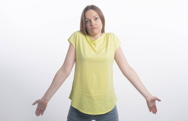 Clueless young woman dressed in casual clothing shrugging shoulders and staring at camera with confused look after she did something wrong but not feeling sorry or guilty at all, studio - Photo, image
