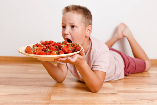 The baby wants to eat a lot of strawberries. hilarious photo of a boy and berries. big appetite - Zdjęcie, obraz