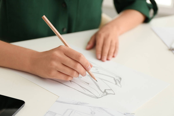 Mujer dibujando ropa con lápiz en hoja de papel en la mesa blanca, primer plano - Foto, Imagen